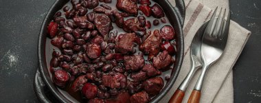 Feijoada, dökme demir bir tencerede geleneksel Brezilya güveci, keten peçetede çatal ve kaşıkla servis edilmeye hazır.