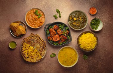 Kahverengi masadaki çeşitli Hint yemeklerinin genel görünümü, köri, tandır tavuğu, tavuk tikka masala, dal, Palak paneer, paratha, pirinç, samosa, Hindistan 'ın zengin aşçılık mirası