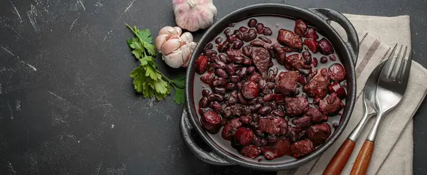 Feijoada, dökme demir bir tencerede geleneksel Brezilya güveci, yanında taze sarımsak ve maydanoz, keten peçetede çatal ve kaşıkla servis edilmeye hazır,
