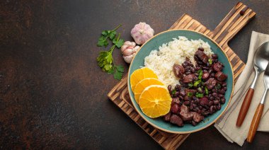 Siyah fasulye, domuz eti, pirinç ve portakal dilimli Brezilya usulü güveç ahşap tahtada çatal bıçak ve peçeteyle servis edilir. Brezilya 'nın geleneksel yemeği