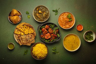 Yeşil masadaki çeşitli Hint yemeklerinin genel görünümü, köri, tandır tavuğu, tavuk tikka masala, dal, Palak paneer, paratha, pirinç, samosa, Hindistan 'ın zengin mutfak mirası