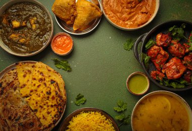 Yeşil bir masadaki çeşitli Hint yemeklerinin genel görünümü, köri, tandır tavuğu, tavuk tikka masala, dal, Palak paneer, paratha, pilav, samosa gibi. Hindistan mutfağı, kopyalama alanı