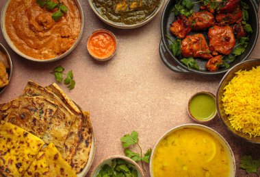 Köri, tandır tavuğu, tavuk tikka masala, dal, Palak paneer, paratha, pilav, samosa dahil olmak üzere bej masadaki çeşitli Hint yemeklerinin genel görünümü. Hindistan mutfağı, kopyalama alanı