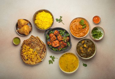 Köri, tandır tavuğu, tavuk tikka masala, dal, Palak paneer, paratha, pirinç, samosa, Hindistan 'ın zengin aşçılık mirası dahil olmak üzere bej bir masadaki çeşitli Hint yemeklerinin genel görünümü