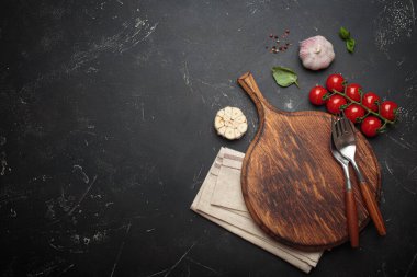 Kiraz domatesleri, sarımsak ve taze fesleğen yaprakları ahşap bir kereste kesme tahtasının üzerinde, ahşap bir biber değirmeninin yanında, koyu renkli bir arka plan, kopyalama alanı.