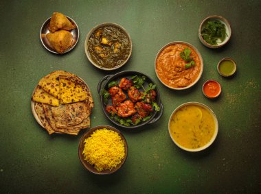 Yeşil masadaki çeşitli Hint yemeklerinin genel görünümü, köri, tandır tavuğu, tavuk tikka masala, dal, Palak paneer, paratha, pirinç, samosa, Hindistan 'ın zengin mutfak mirası