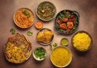 Kahverengi masadaki çeşitli Hint yemeklerinin genel görünümü, köri, tandır tavuğu, tavuk tikka masala, dal, Palak paneer, paratha, pirinç, samosa, Hindistan 'ın zengin aşçılık mirası