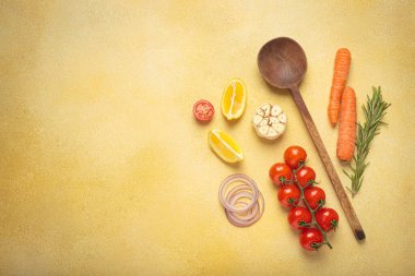 Kiraz domatesleri, sarımsak, limon dilimleri, havuç, kırmızı soğan ve biberiye filizi sarı bir arka planda ahşap bir kaşık, aşçılık yaratıcılığı ve sağlıklı beslenme konsepti, kopyalama alanı.