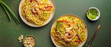 İki tabak Tayland eriştesi, karides, fıstık, limon, biber ve yeşil zemin üzerinde taze soğan ve yemek çubukları ve kabın içindeki malzemelerle. Geleneksel Tayland yemekleri