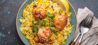 Lezzetli Hintli tavuk biryanisi tavukla süslenmiş taze kişniş ve limonla süslenmiş, kırsal bir masada, yanında çatal bıçakla birlikte. Hindistan 'ın otantik yemeği