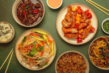 Çeşitli Çin yemekleri, tatlı ve ekşi tavuk, soslu sığır eti, erişte, kızarmış pirinç, salata ve ahşap çubuklar. Çin ya da Asya restoranı konsepti