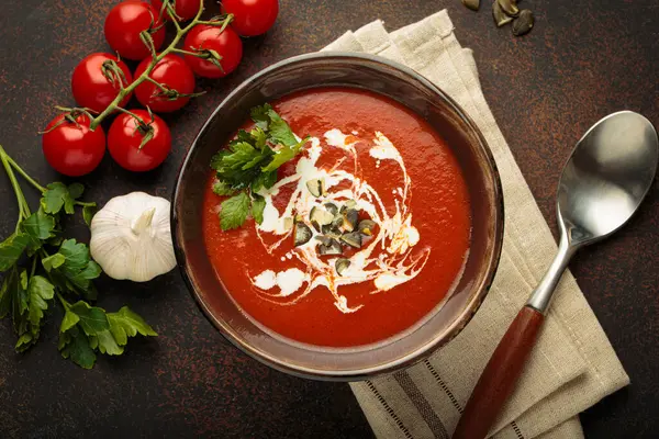 Taze domates çorbası krema, tohum ve otlarla dolu bir kasede servis edilir. Yanında da kaşık ve peçeteyle birlikte kiraz domatesleri, sarımsak ve maydanoz bulunur.