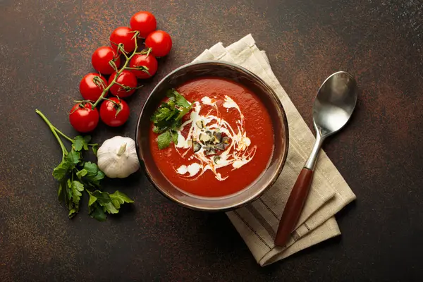 Taze domates çorbası krema, tohum ve otlarla dolu bir kasede servis edilir. Yanında da kaşık ve peçeteyle birlikte kiraz domatesleri, sarımsak ve maydanoz bulunur.