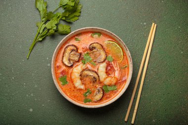 Karides, mantar, limon ve kişniş karışımlı lezzetli Tom çorbası mavi arka planda yemek çubuklarıyla servis edilen Tayland aromalı geleneksel bir yemektir.