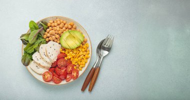 Izgara tavuk göğsü, avokado, nohut, mısır, domates ve karışık sebzeli sağlıklı kase, yukarıdan gri arka plan, dengeli ve besleyici bir yemek.