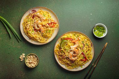 İki tabak Tayland eriştesi, karides, fıstık, limon, biber ve yeşil zemin üzerinde taze soğan ve yemek çubukları ve kabın içindeki malzemelerle. Geleneksel Tayland yemekleri