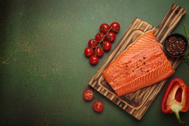 Tahta kesme tahtasındaki taze çiğ somon filetosu yanında da vişneli domates, maydanoz ve dolmalık biber. Aşçılık İçindekiler yeşil rustik arkaplan görünümünde düzenlendi, boşluk kopyala