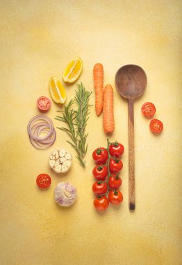 Kiraz domatesleri, sarımsak, limon dilimleri, havuç, kırmızı soğan ve biberiye filizi sarı bir zemin üzerinde ahşap kaşık, aşçılık yaratıcılığı ve sağlıklı beslenme konsepti ile birlikte sıralanmış.
