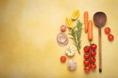 Kiraz domatesleri, sarımsak, limon dilimleri, havuç, kırmızı soğan ve biberiye filizi sarı bir arka planda ahşap bir kaşık, aşçılık yaratıcılığı ve sağlıklı beslenme konsepti, kopyalama alanı.