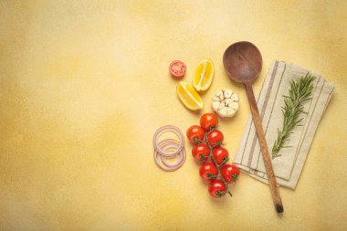Kiraz domatesleri, sarımsak, limon dilimleri, havuç, kırmızı soğan ve biberiye filizi sarı bir arka planda ahşap bir kaşık, aşçılık yaratıcılığı ve sağlıklı beslenme konsepti, kopyalama alanı.