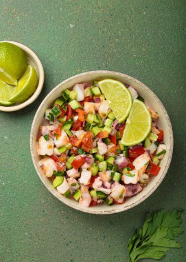 Taze ve canlı Peru deniz ürünleri ceviche ile karides, ahtapot, domates, salatalık ve maydanoz, yukarıdan yeşil bir arka planda limonla servis edilmiş, Peru yemeği.
