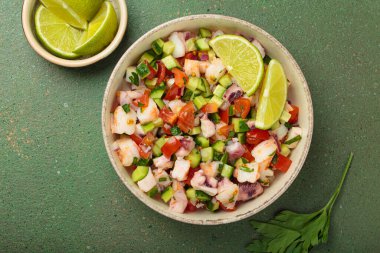 Taze ve canlı Peru deniz ürünleri ceviche ile karides, ahtapot, domates, salatalık ve maydanoz, yukarıdan yeşil bir arka planda limonla servis edilmiş, Peru yemeği.