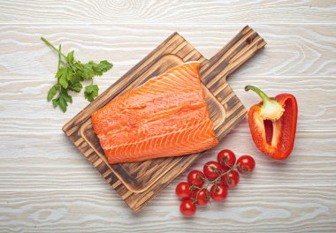 Biberli taze somon filetosu yanında vişneli domates, kırmızı dolmalık biber ve maydanoz. Beyaz ahşap arka planda sağlıklı yemek malzemeleri. Üst görünüm bileşimi