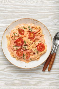 Taze maydanozla süslenmiş karides ve kiraz domatesli kaymak soslu deniz ürünleri linguine makarna beyaz ahşap arka planda servis edilir.