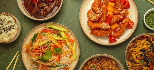 Çeşitli Çin yemekleri, tatlı ve ekşi tavuk, soslu sığır eti, erişte, kızarmış pirinç, salata ve ahşap çubuklar. Çin ya da Asya restoranı konsepti