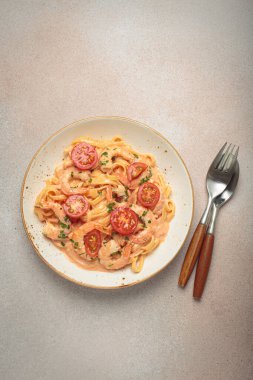 Taze maydanozla süslenmiş karides ve kiraz domatesli kaymak soslu deniz ürünleri linguine makarna, açık bej arka planda servis edilir.