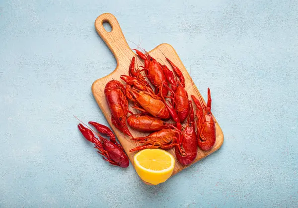 Tahta kesme tahtasının üzerinde birkaç kırmızı kerevit ve mavi dokulu arka planda yukardan çekilmiş bir dilim limon var.