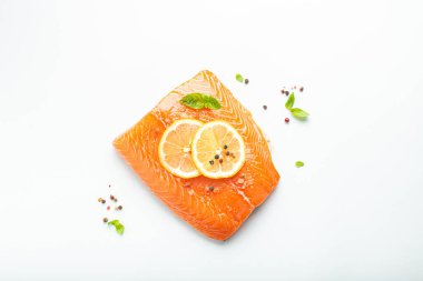 Taze çiğ somon balığı filetosu beyaz arka planda limon, kaba tuz ve yeşil otlarla izole edilmiş. Sağlıklı beslenme ve dengeli beslenme.