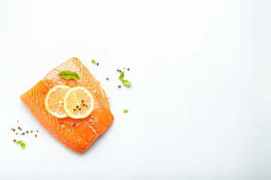 Taze çiğ somon balığı filetosu beyaz arka planda limon, kaba tuz ve yeşil otlarla izole edilmiş. Sağlıklı beslenme ve dengeli diyet. Metin için boşluk.