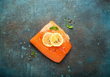 Taze çiğ somon filetosu koyu mavi kırsal beton masa arka planında limon, kaba tuz, yeşil otlar üst manzara. Sağlıklı yemek ve dengeli beslenme.