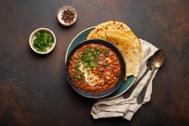 Geleneksel Hint Punjabi yemeği mercimek ve siyah kasede fasulye ile Dal Makhani naan düz ekmek, taze kişniş ve kahverengi beton kırsal masa manzaralı iki kaşık ile servis edilir..