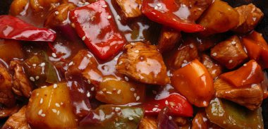 Tatlı ve ekşi domuz eti ve dolmalık biber ve ananas tavada pişiyor, susam tohumlarıyla serpiştirilmiş. Bu yemek lezzet ve renkle dolu.