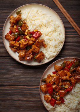 İki tabak Çin kung pao tavuğu, pilav, sebze ve baharatlı soslu fıstık. Ahşap arka planda üst manzara. Öğle veya akşam yemeği için mükemmel.