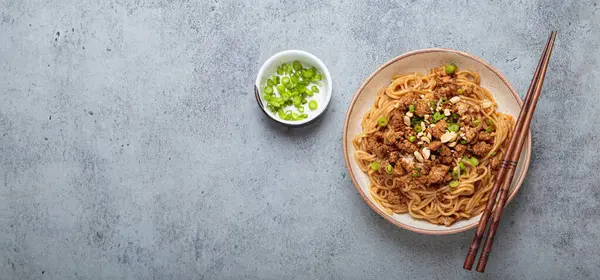 Dan Dan erişteleri yemek çubukları ve yeşil soğanla servis ediliyor. Sichuan mutfağının leziz lezzetlerini sergiliyorlar.