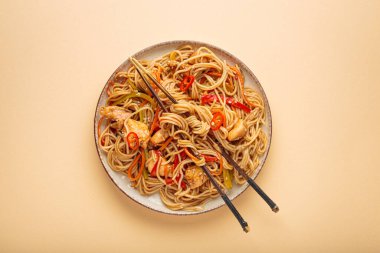 Kızarmış erişteyi teriyaki tavuğu ve sebzeyle karıştır yemek çubuklarıyla bir tabakta, bej arka plan manzaralı