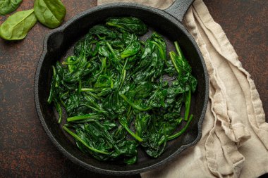 Taze buğulanmış ıspanak yaprakları dökme demir bir tavada, besleyici ve lezzetli bir meze veya sağlıklı yemekler için malzeme olarak servis edilir.