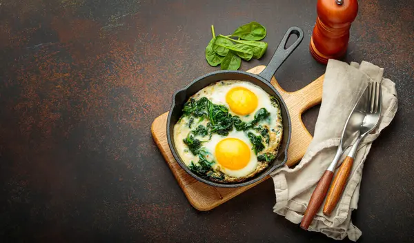 Tahta bir tahtanın üzerinde ıspanaklı iki sahanda yumurta, sağlıklı bir kahvaltı.