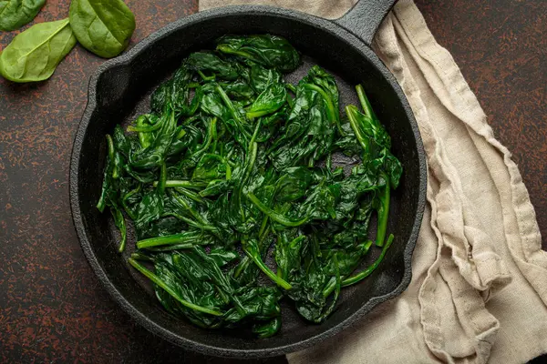 Taze buğulanmış ıspanak yaprakları dökme demir bir tavada, besleyici ve lezzetli bir meze veya sağlıklı yemekler için malzeme olarak servis edilir.