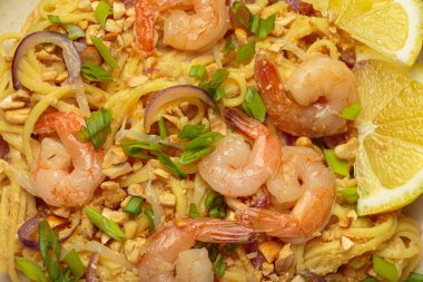 Lezzetli Tayland eriştelerine yakın pişmiş karides, kavrulmuş fıstık, doğranmış yeşil soğan, kırmızı soğan halkaları ve limon dilimi, geleneksel Tayland yemeği.