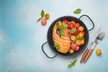 Siyah tavada ızgara somon bifteği, yanında canlı vişne domatesleri ve taze fesleğen yaprakları, sağlıklı beslenme ya da diyet konsepti, kopyalama alanı.