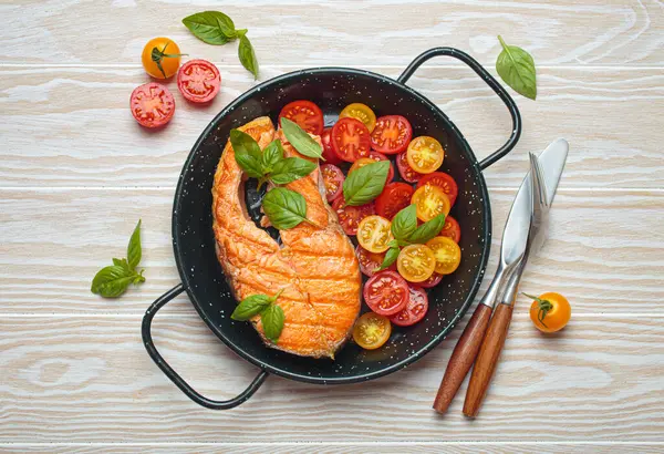 Siyah tavada ızgara somon bifteği, yanında canlı kiraz domatesleri ve taze fesleğen yaprakları, sağlıklı beslenme ya da diyet konsepti.