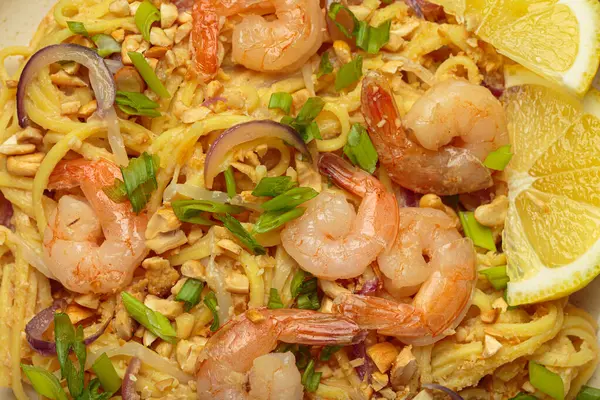 Lezzetli Tayland eriştelerine yakın pişmiş karides, kavrulmuş fıstık, doğranmış yeşil soğan, kırmızı soğan halkaları ve limon dilimi, geleneksel Tayland yemeği.