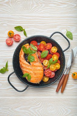 Siyah tavada ızgara somon bifteği, yanında canlı kiraz domatesleri ve taze fesleğen yaprakları, sağlıklı beslenme ya da diyet konsepti.