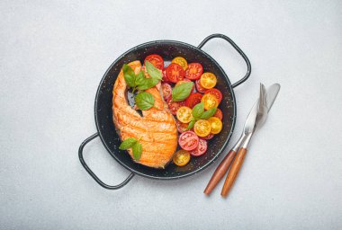 Siyah tavada ızgara somon bifteği, yanında canlı kiraz domatesleri ve taze fesleğen yaprakları, sağlıklı beslenme ya da diyet konsepti.