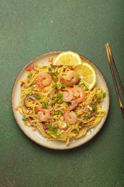 Karides, fıstık, yeşil soğan, limon dilimleri ile süslenmiş Tayland erişteleri ve kırsal yeşil arka planda servis edilen çubuklarla Tayland mutfağı.