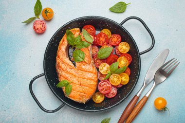 Siyah tavada ızgara somon bifteği, yanında canlı kiraz domatesleri ve taze fesleğen yaprakları, sağlıklı beslenme ya da diyet konsepti.